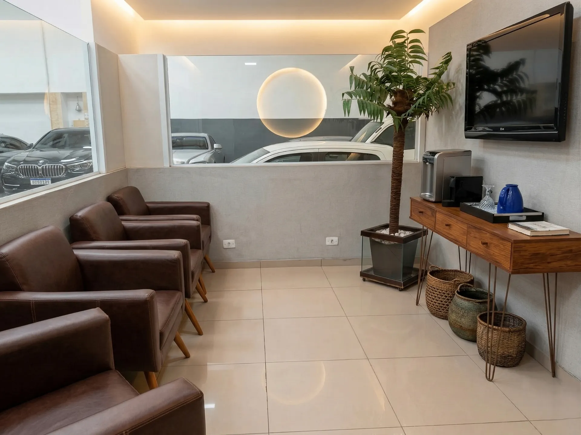 Sala de espera com poltronas, televisão e vista para a área de serviço.